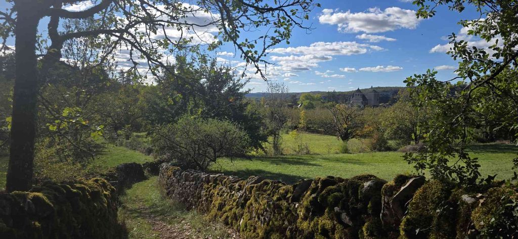 Chemin de randonnée à Floirac dans le Lot Sentier bordé de murets en pierres couvertes de mousse, avec une vue sur la campagne et le village de Floirac
